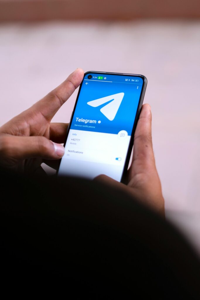 Close-up of hands holding a smartphone with the Telegram app open on the screen.